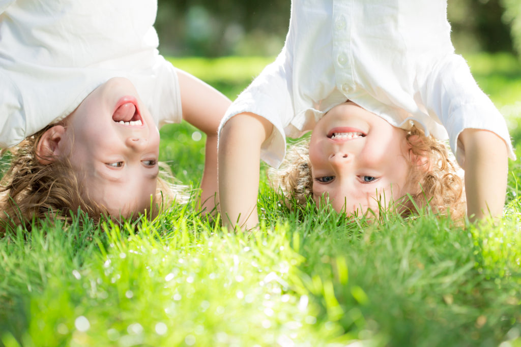 Happy,Children,Standing,Upside,Down,On,Green,Grass,In,Spring